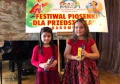 Dwie uczestniczki konkursu stoją na tle napisu Festiwal Piosenki dla Przedszkolaka.